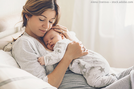 Frau liegt mit Baby im Arm im Bett